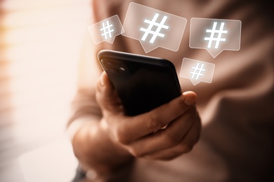 Man using modern smartphone, closeup. Hashtag symbols over device