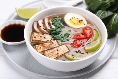 Delicious vegetarian ramen in bowl and soy sauce on white table, closeup