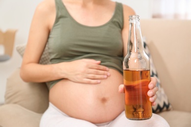 Photo of Pregnant woman with bottle of whiskey at home. Alcohol addiction