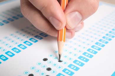 Student filling answer sheet at table, closeup. Passing exam