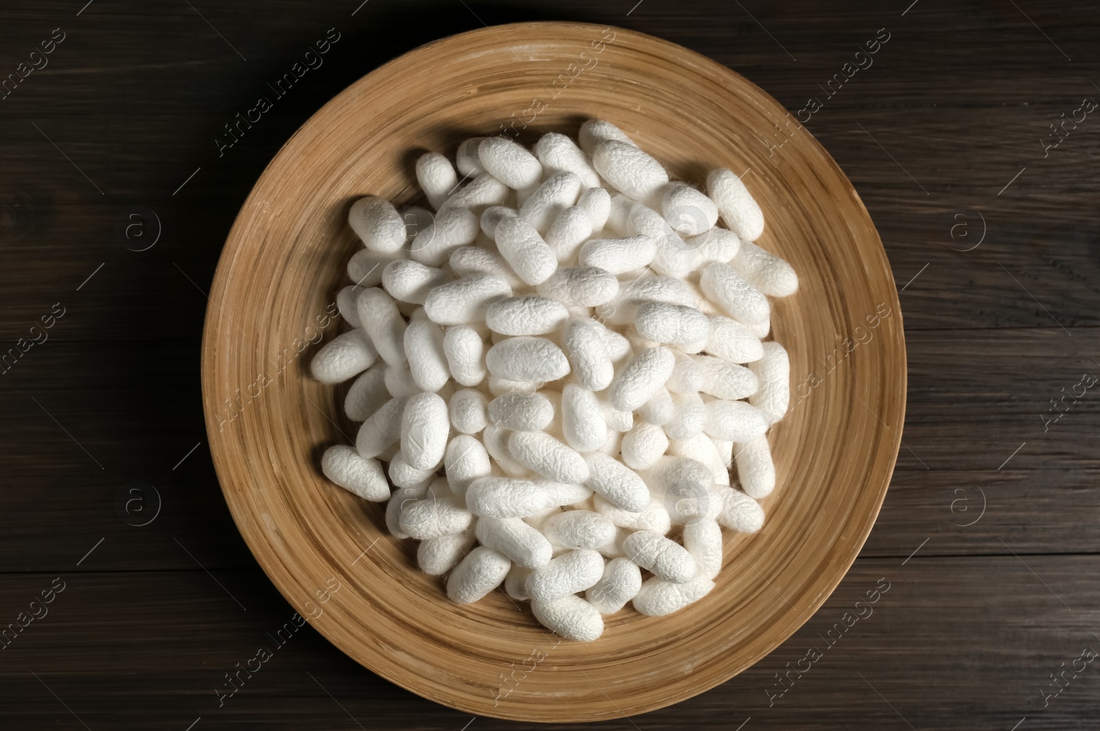 Photo of White silk cocoons with plate on wooden table, top view