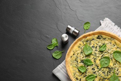 Photo of Delicious homemade spinach pie with spices on black table, flat lay. Space for text