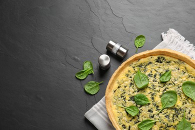 Delicious homemade spinach pie with spices on black table, flat lay. Space for text