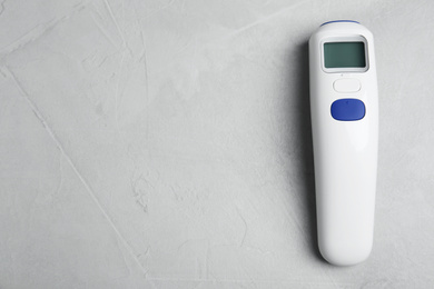 Photo of Modern non-contact infrared thermometer on light grey stone background, top view. Space for text