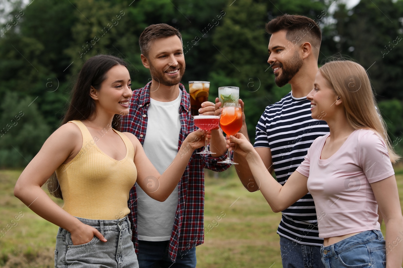 Photo of Happy friends clinking glasses with cocktails outdoors