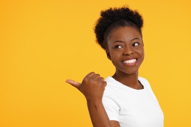 Happy young woman pointing at something on orange background. Space for text