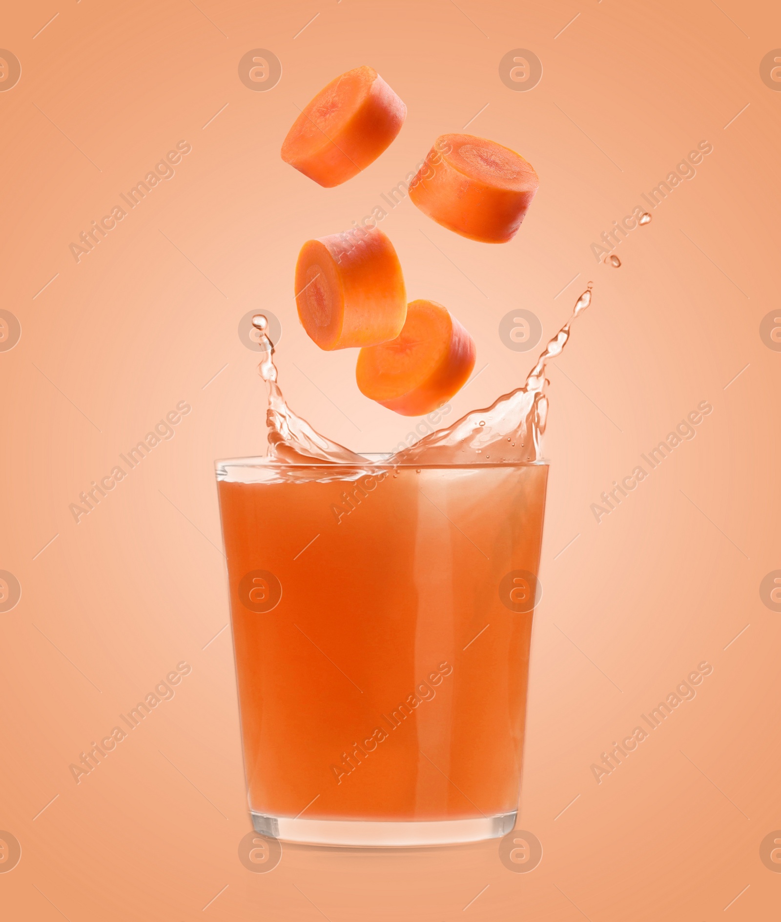 Image of Splashing freshly made carrot juice on coral background. Cut carrot falling into glass