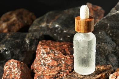 Photo of Bottle of face serum on wet stones, closeup