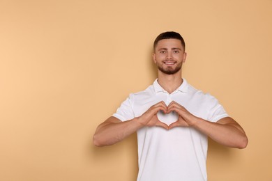 Photo of Happy volunteer making heart with his hands on beige background. Space for text