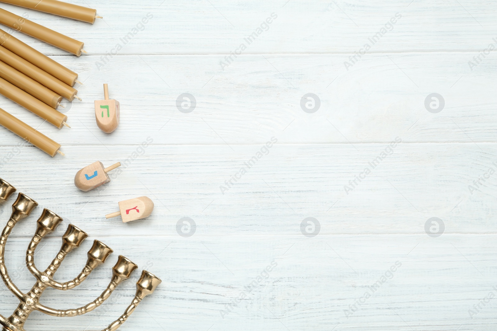 Photo of Golden menorah, yellow candles and Hanukkah dreidels with He, Nun, Gimel symbols on white wooden table, flat lay. Space for text