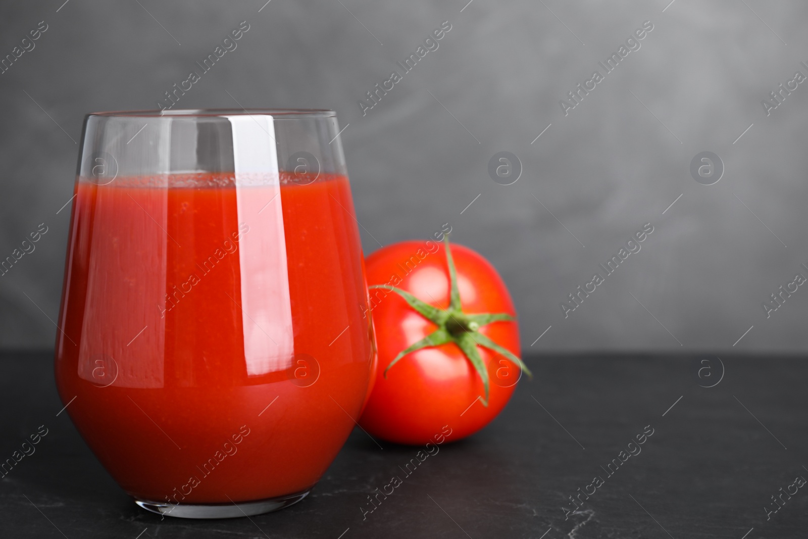 Photo of Delicious fresh tomato juice on black table against grey background, closeup. Space for text