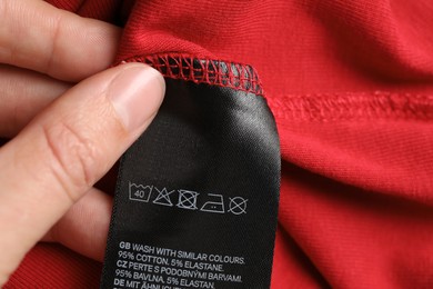 Photo of Woman holding clothing label on red garment, closeup