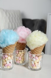 Photo of Sweet cotton candies in waffle cones and marshmallows on white table indoors