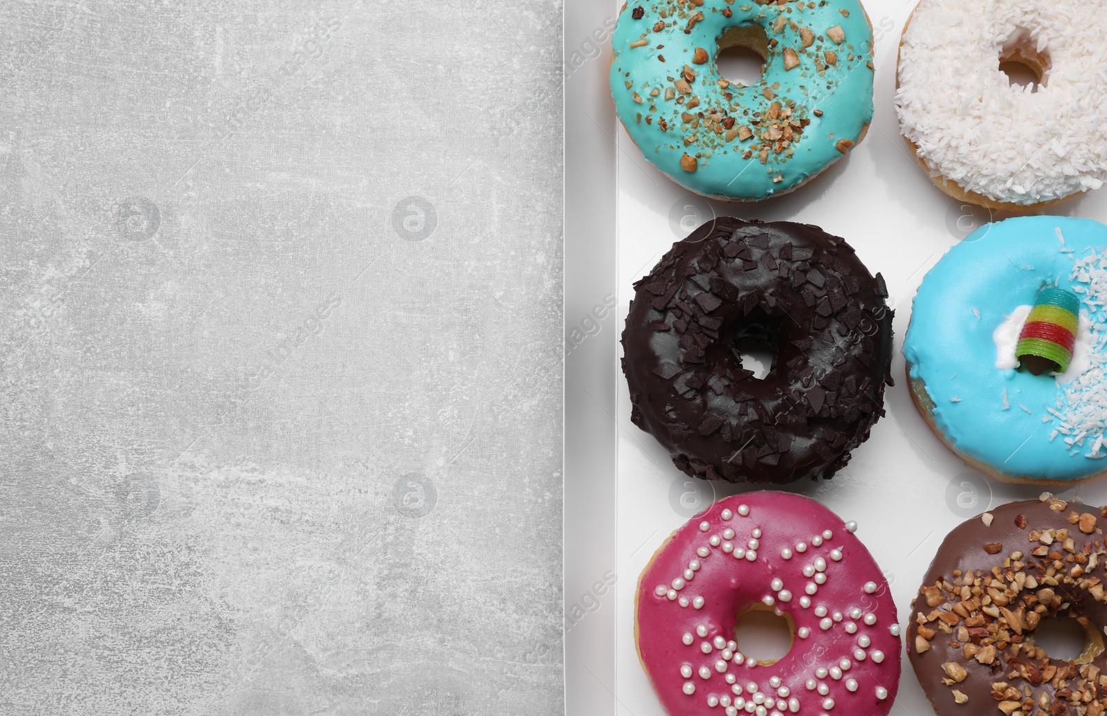 Photo of Box with different tasty glazed donuts on light grey table, top view. Space for text