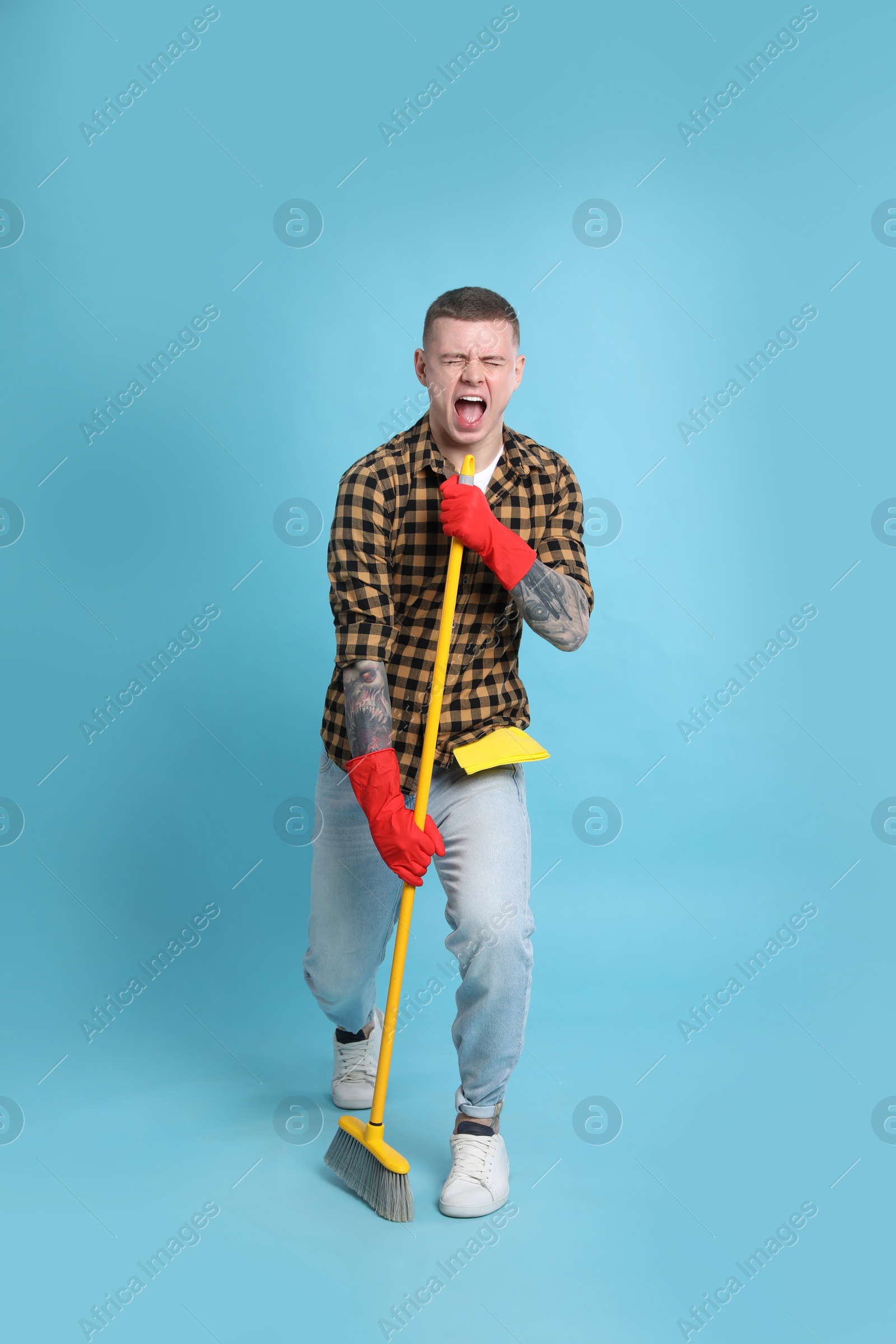 Photo of Handsome young man with floor brush singing on light blue background