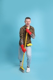 Photo of Handsome young man with floor brush singing on light blue background