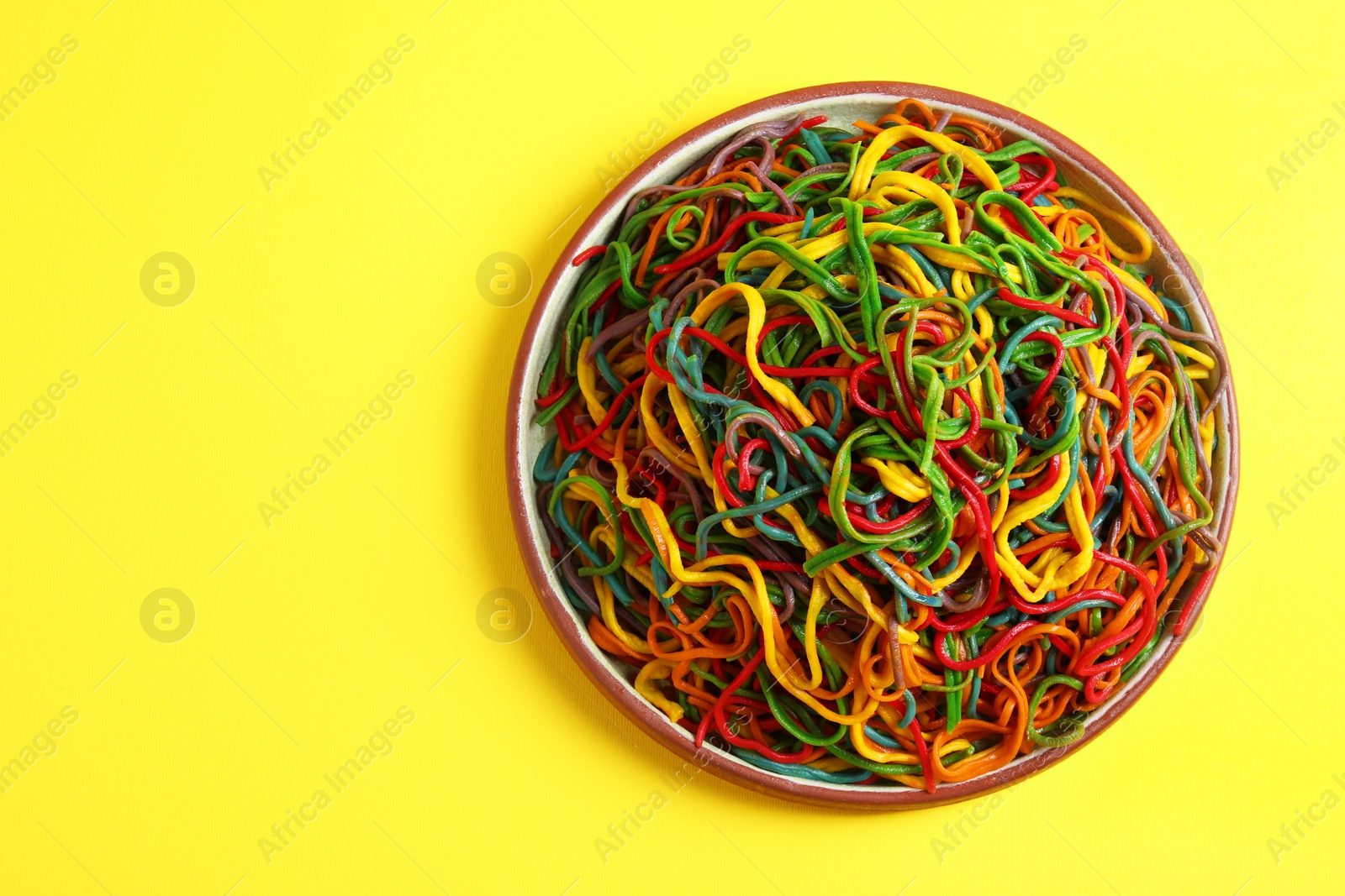 Photo of Plate of spaghetti painted with different food colorings on yellow background, top view. Space for text