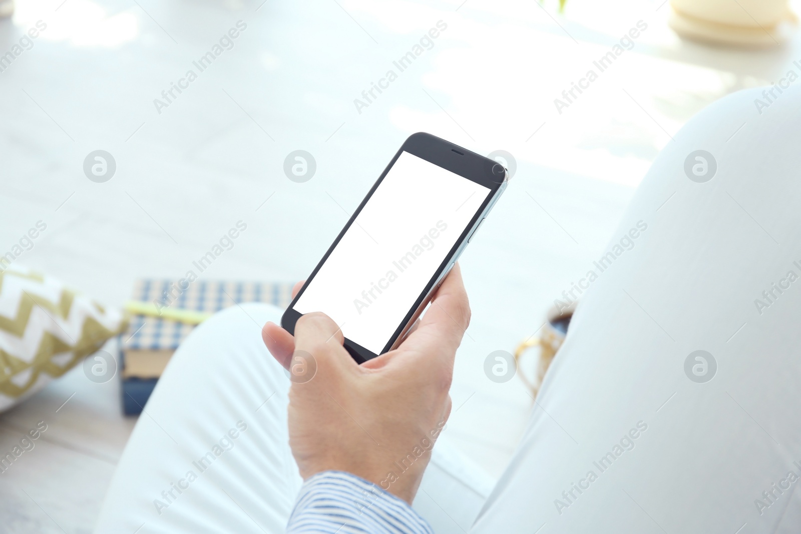 Photo of Young man holding mobile phone with blank screen in hand, indoors