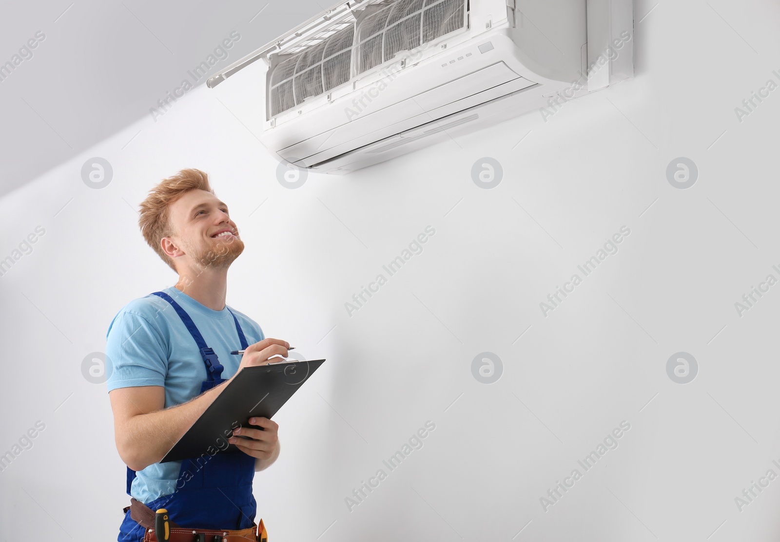 Photo of Professional technician with clipboard near modern air conditioner indoors