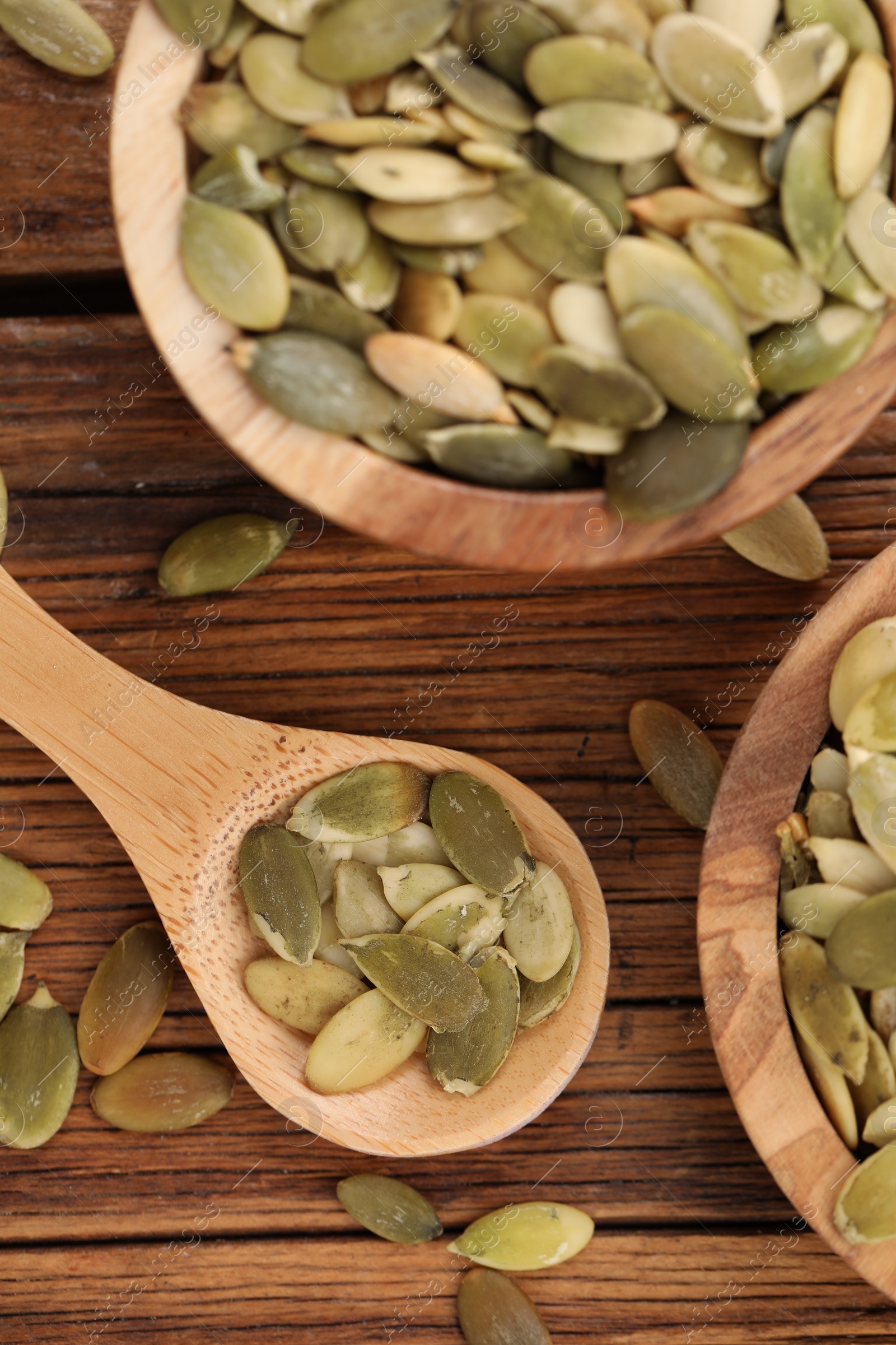 Photo of Bowl and spoon with peeled pumpkin seeds on wooden table, flat lay