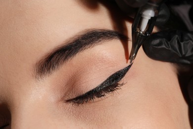Photo of Young woman undergoing procedure of permanent eye makeup in tattoo salon, closeup