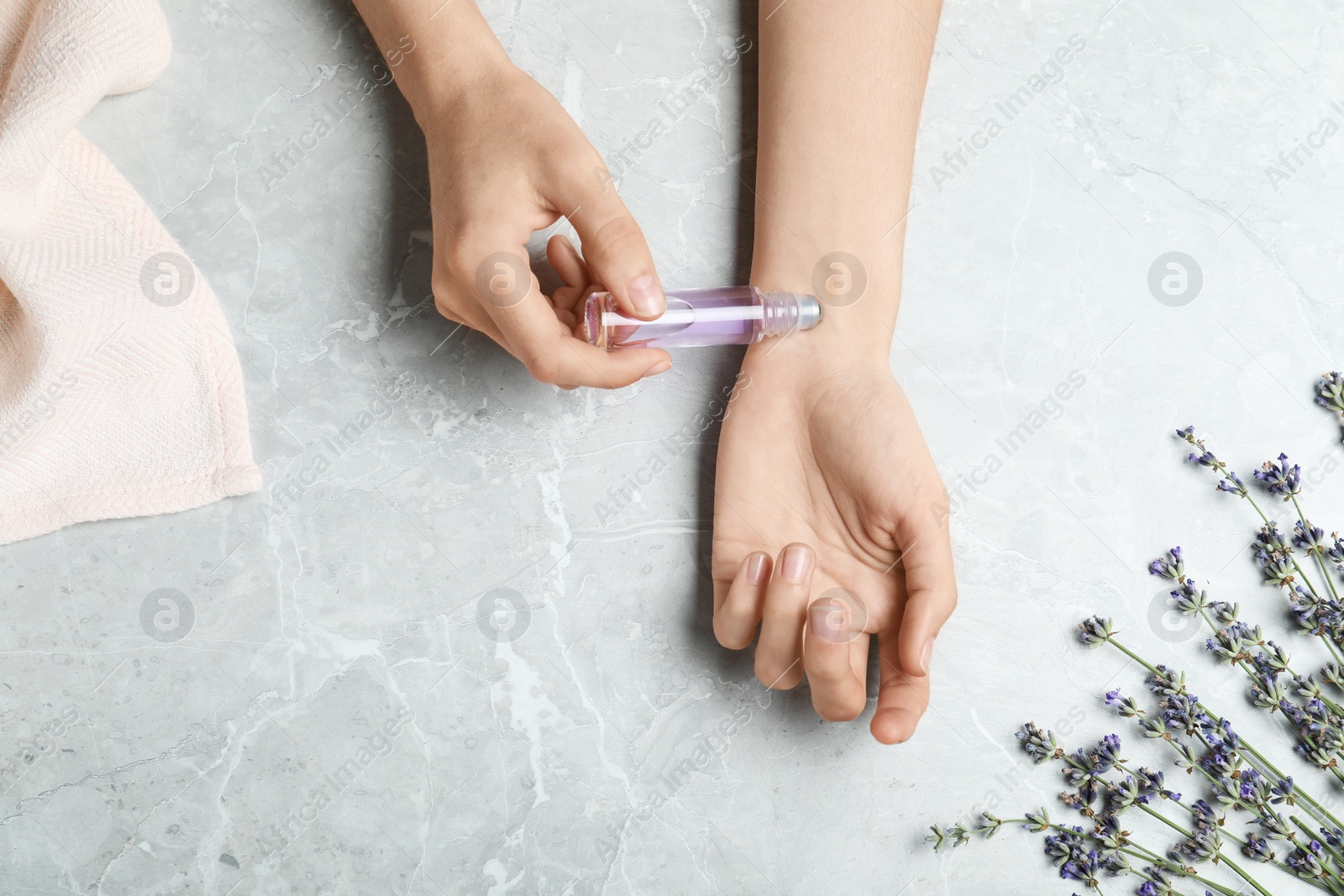 Photo of Top view of woman applying lavender essential oil at stone table, closeup