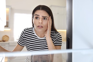 Upset woman near empty refrigerator in kitchen, view from inside