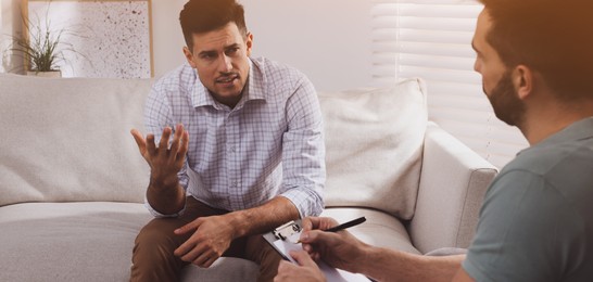 Image of Unhappy man having session with his therapist indoors. Banner design