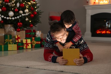 Father and his cute son opening gift box with magical light on floor at home. Christmas celebration
