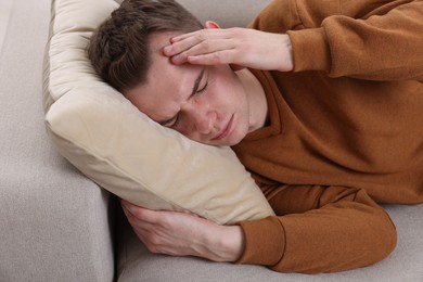 Photo of Sad man suffering from headache on sofa indoors