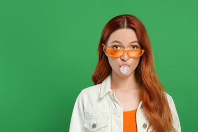 Beautiful woman in sunglasses blowing bubble gum on green background. Space for text