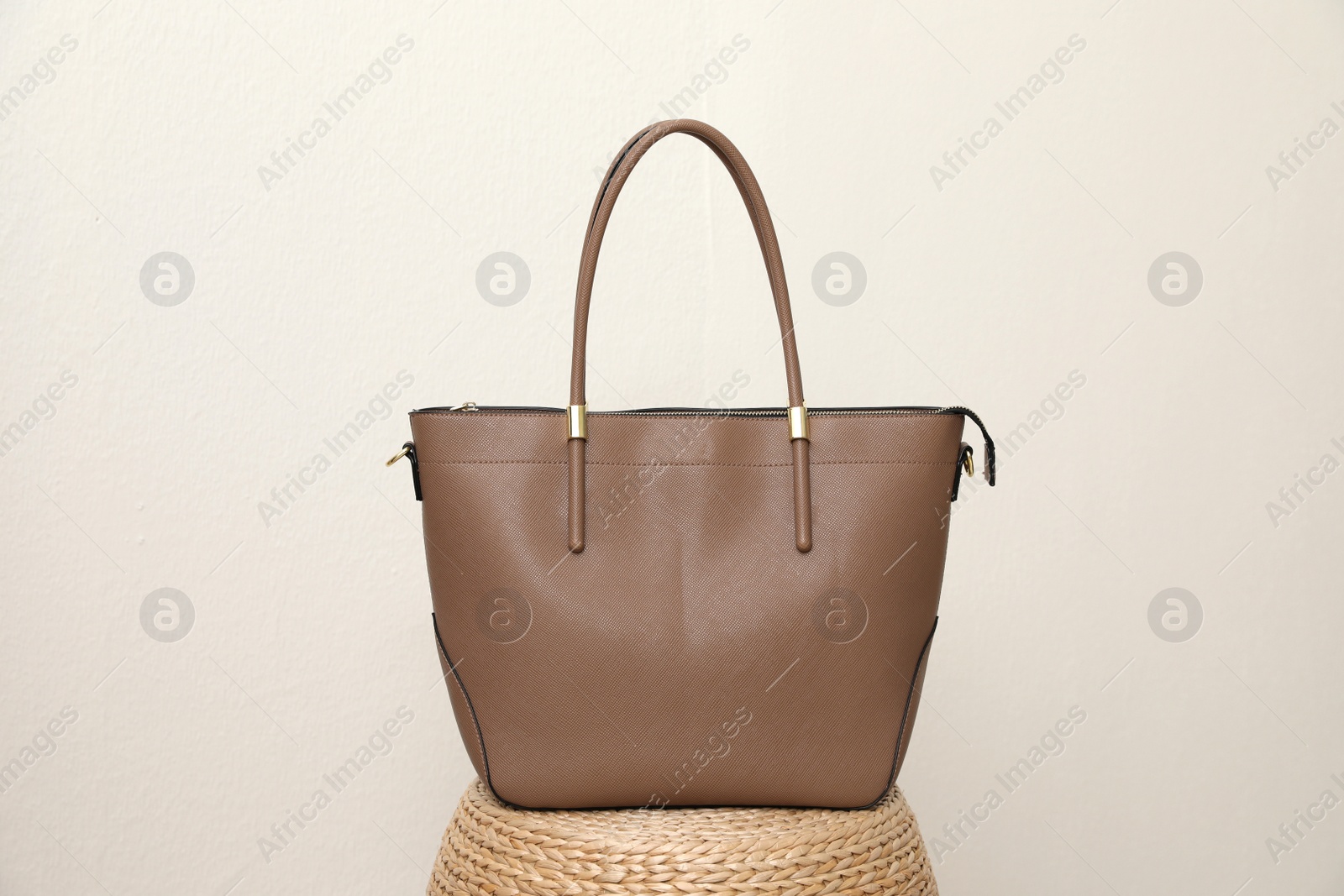 Photo of Stylish woman's bag on wicker stand near light wall