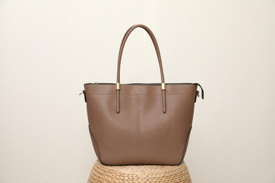 Photo of Stylish woman's bag on wicker stand near light wall