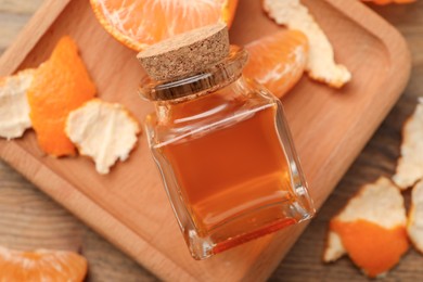 Bottle of tangerine essential oil and peeled fresh fruit on wooden table, top view
