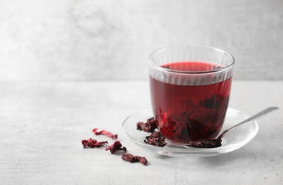Photo of Aromatic hibiscus tea in glass, dried roselle calyces and spoon on light table, space for text