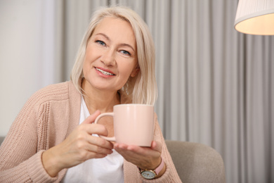 Beautiful mature woman with cup of coffee at home. Space for text
