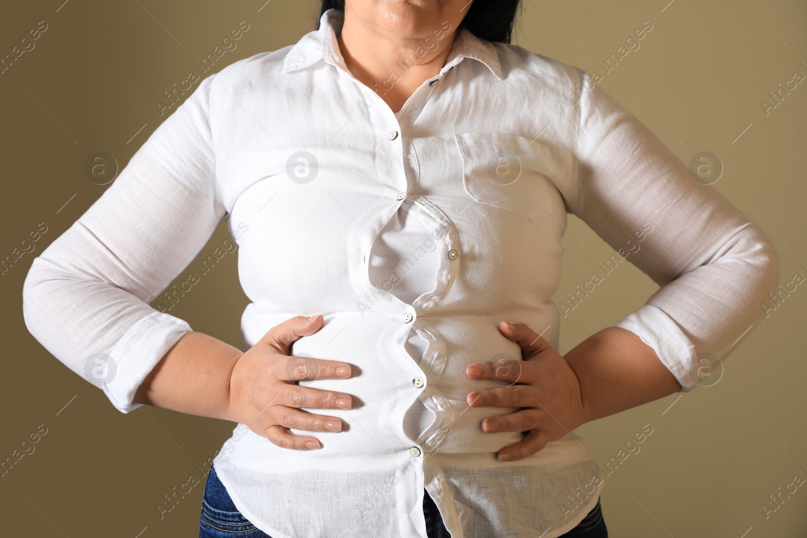 Photo of Overweight woman in tight shirt on light brown background, closeup