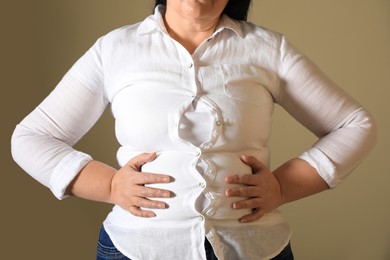 Overweight woman in tight shirt on light brown background, closeup