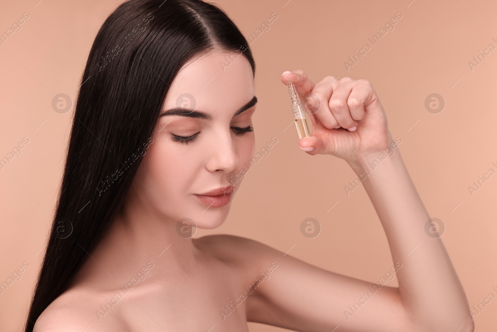 Photo of Beautiful young woman holding skincare ampoule on beige background