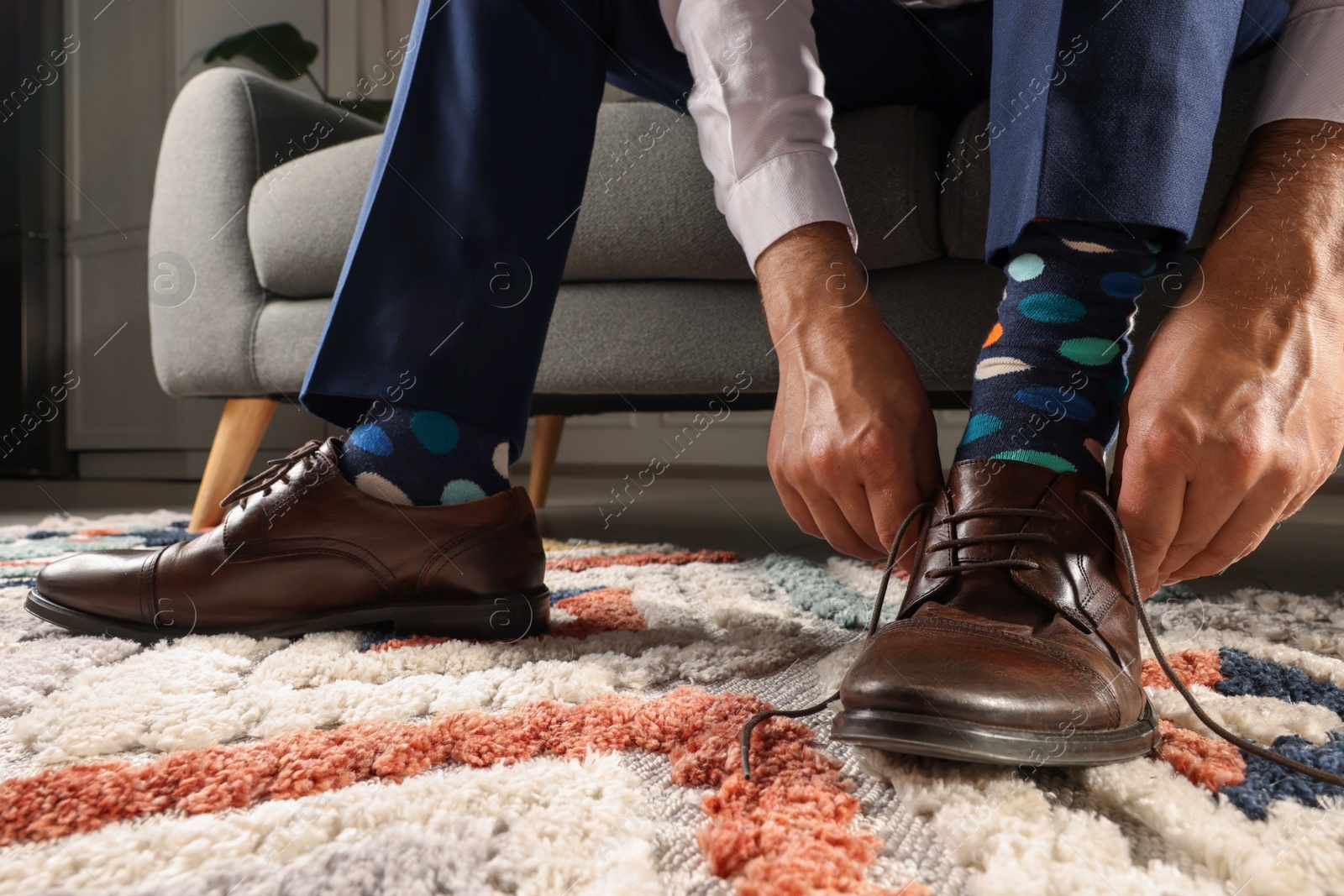 Photo of Man with colorful socks putting on stylish shoes indoors, closeup