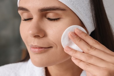 Photo of Young woman cleaning her face with cotton pad indoors, closeup