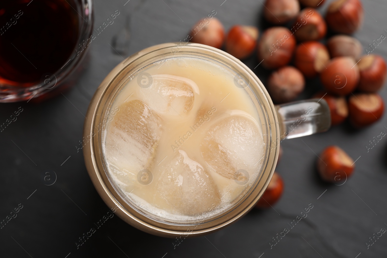 Photo of Mason jar of delicious iced coffee, syrup and hazelnuts on black table, flat lay