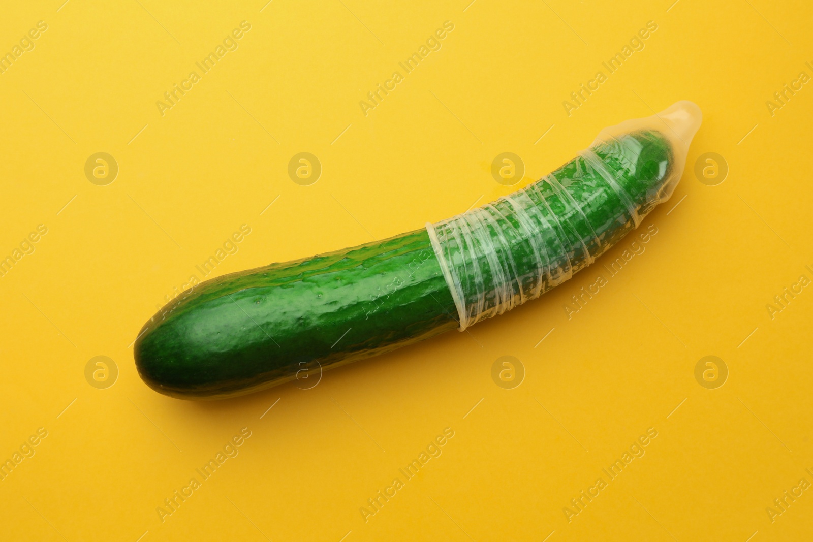 Photo of Cucumber with condom on orange background. Safe sex