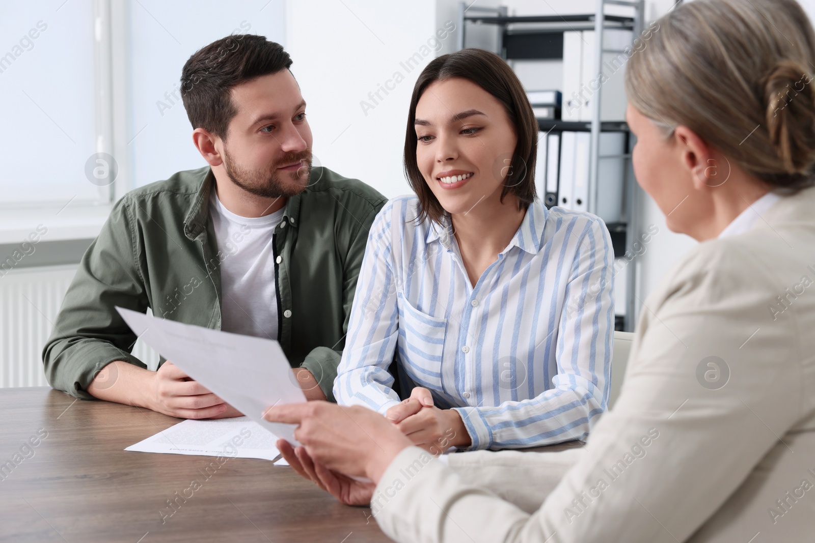 Photo of Young couple consulting insurance agent about pension plan at wooden table indoors