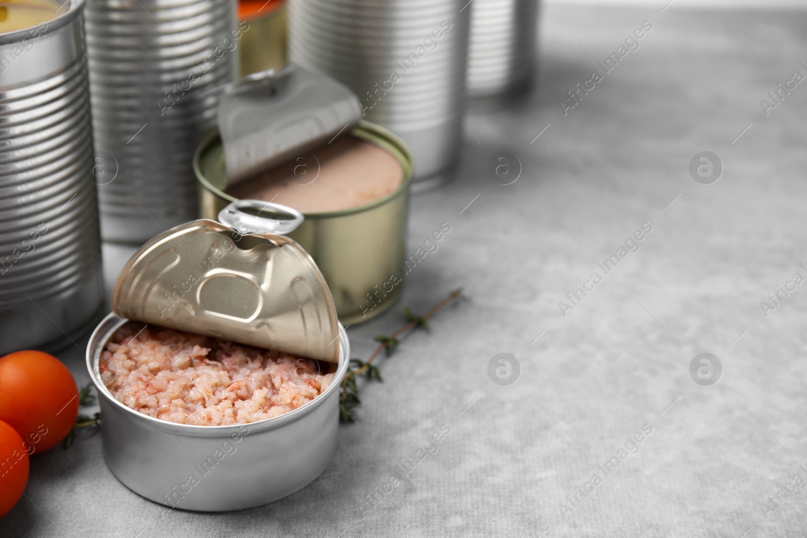 Photo of Open tin cans with different preserved products on grey table, closeup. Space for text