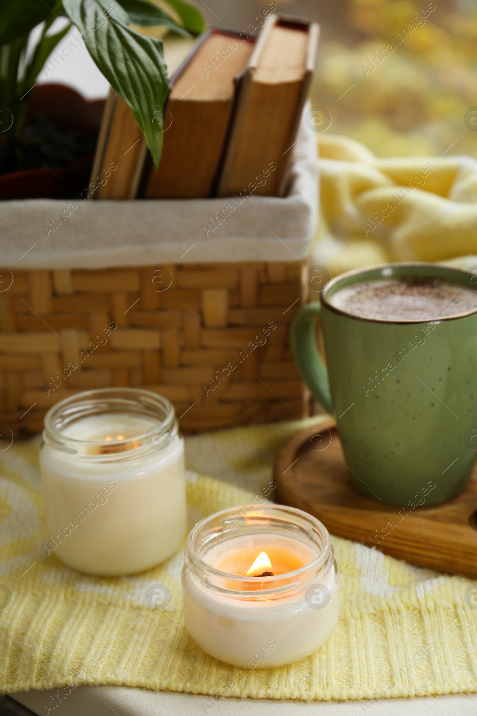 Photo of Burning aromatic candles, cup with hot drink and books on windowsill indoors. Autumn coziness