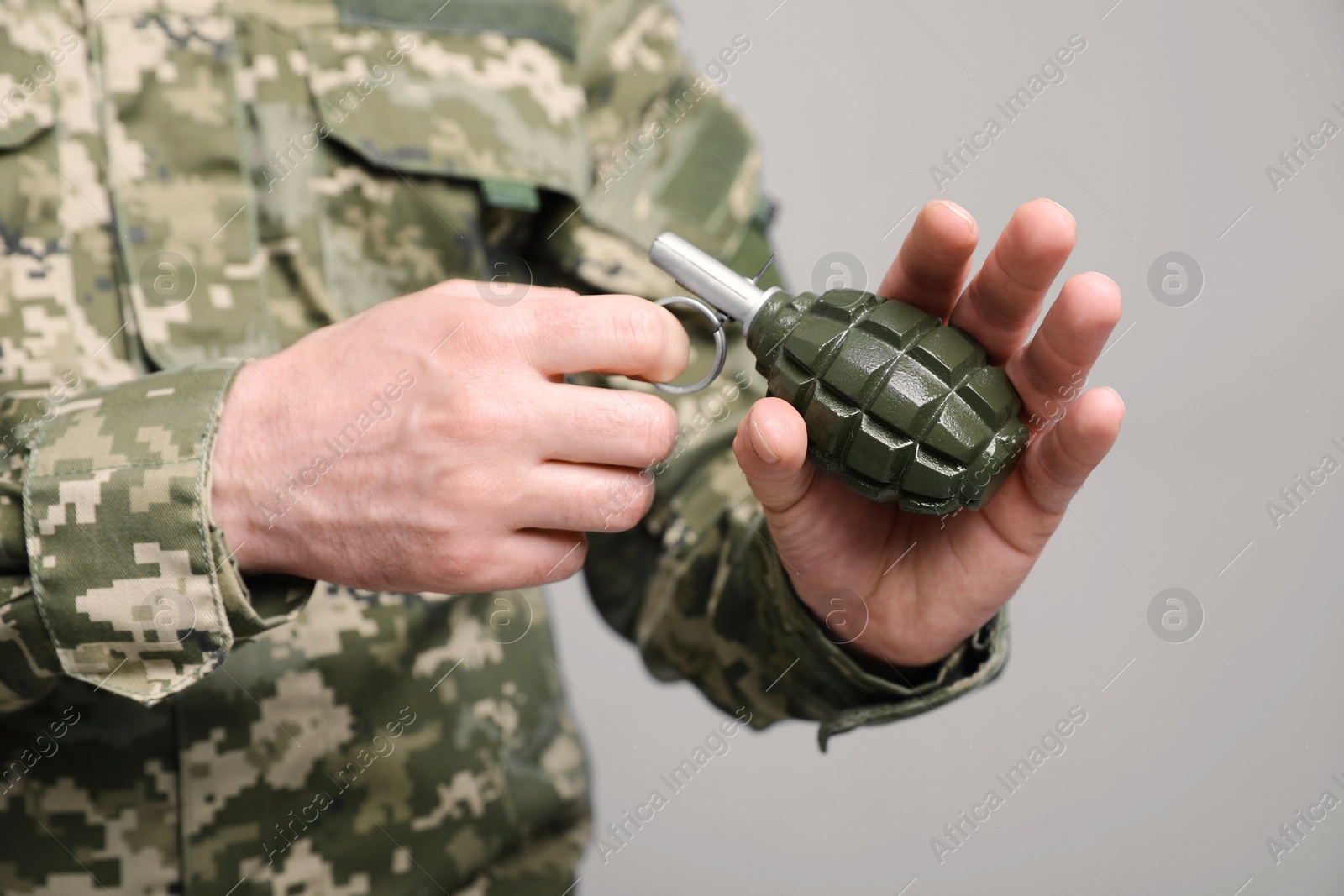 Photo of Soldier pulling safety pin out of hand grenade on light grey background, closeup. Military service