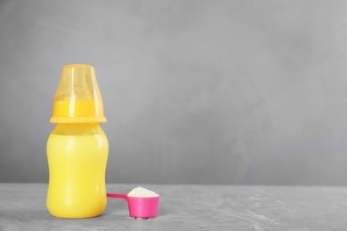 Photo of Feeding bottle with infant formula and scoop of powder on grey table, space for text. Baby milk