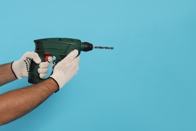 Photo of Worker in gloves with power drill on light blue background, closeup. Space for text