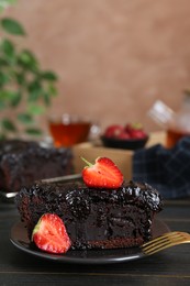 Piece of tasty chocolate sponge cake with strawberries on black wooden table, closeup